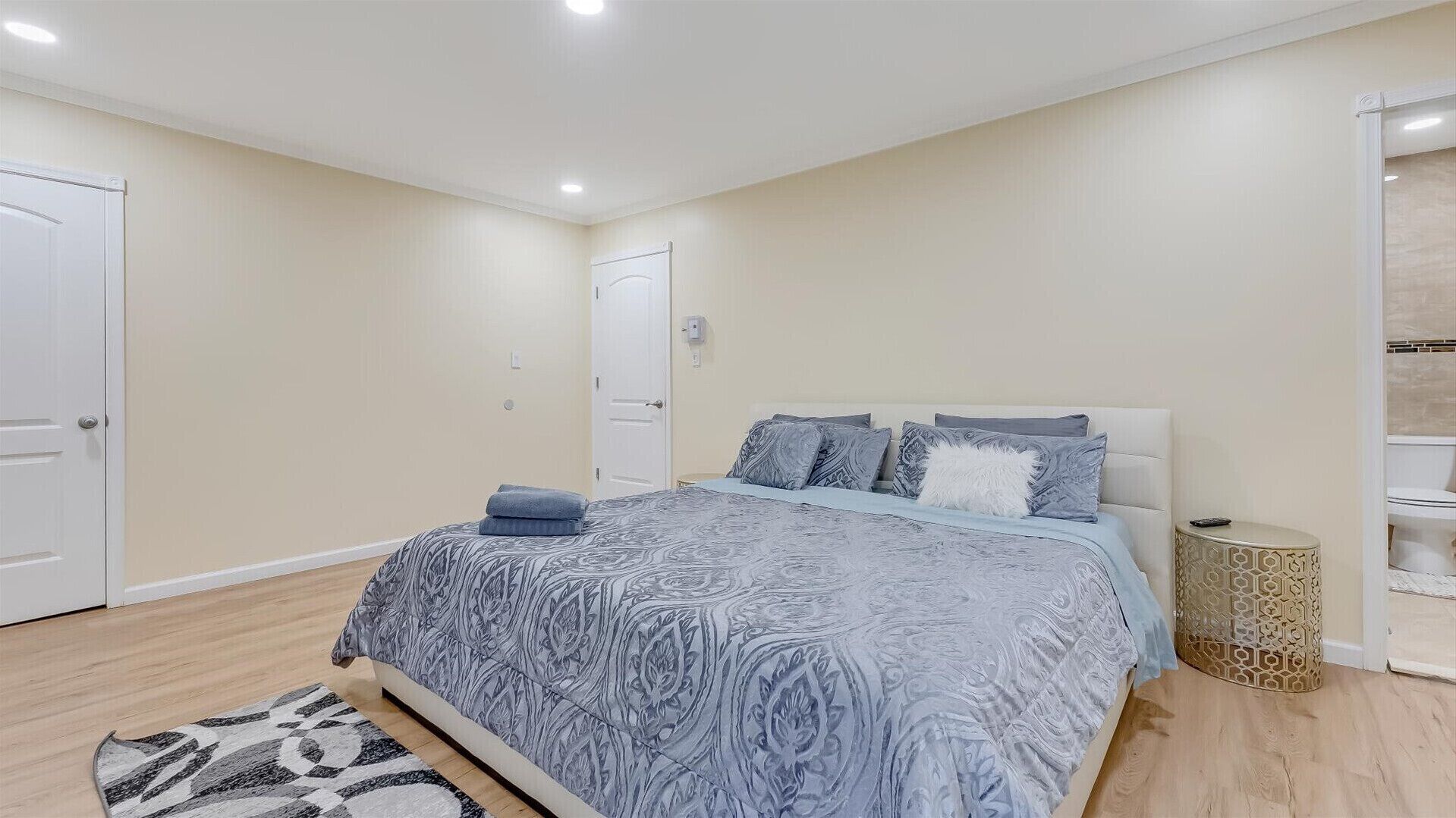 A bedroom with a bed, a bedside table, a rug, and a wall-mounted shelf.