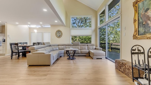 A spacious living room with a large L-shaped sectional sofa, a dining area with a table and chairs, and a view of a deck through large windows.