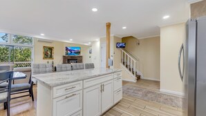 A modern kitchen with a marble countertop, a built-in island with drawers, a stainless steel refrigerator, and a fireplace.