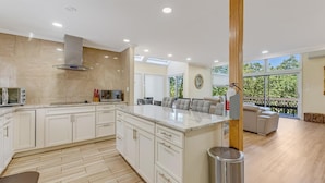 A modern kitchen with white cabinetry, a large island, and a dining area with a sofa and chairs.
