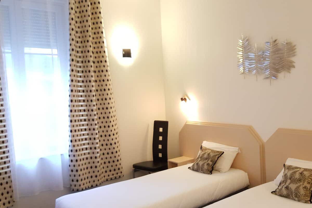 Ein Hotelzimmer mit zwei Betten, einem Nachttisch, einem Sessel und einer Wandleuchte.