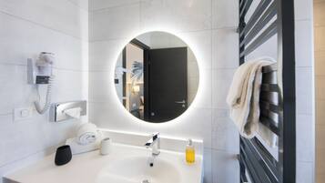 A modern bathroom with a round mirror, a sink, a towel rack, a telephone, and a soap dispenser.
