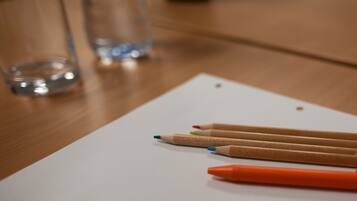 Ein Holztisch mit einem weißen Papierbogen, mehreren farbigen Stiften und einem orangefarbenen Stift.