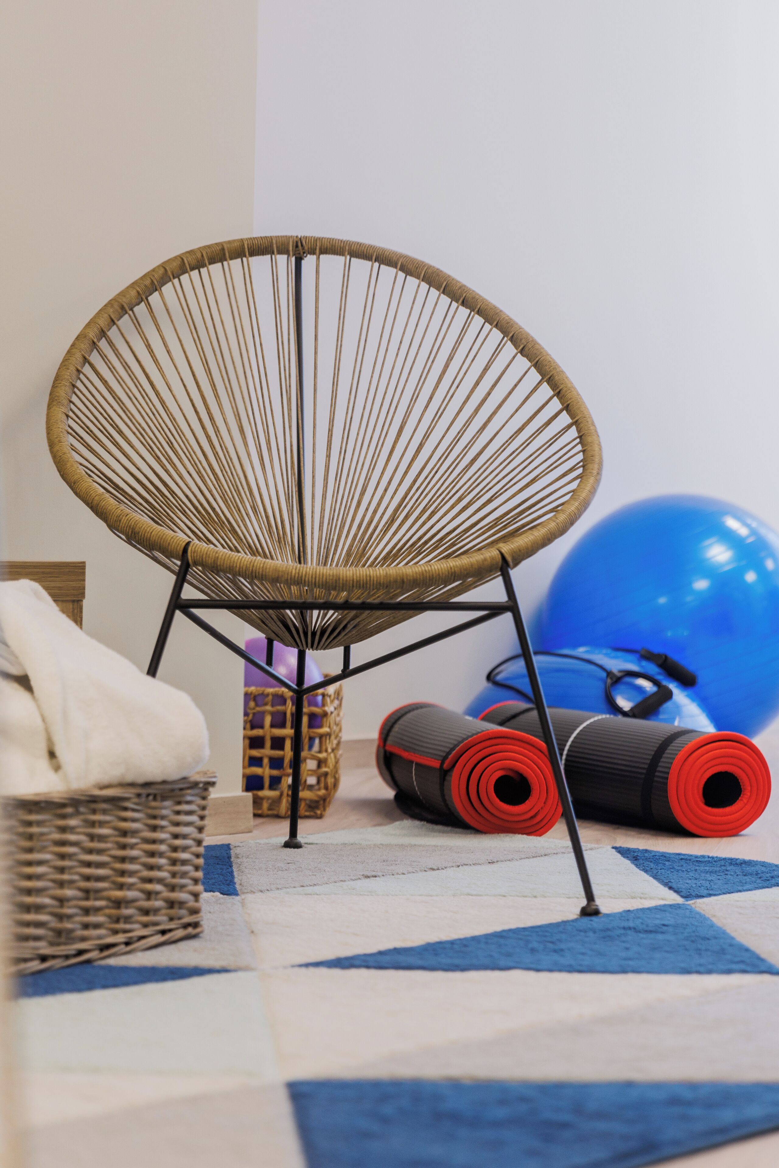 Une pièce comprenant un fauteuil en osier, du matériel d’exercice et un tapis à motifs.