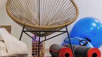 Une pièce comprenant un fauteuil en osier, du matériel d’exercice et un tapis à motifs.