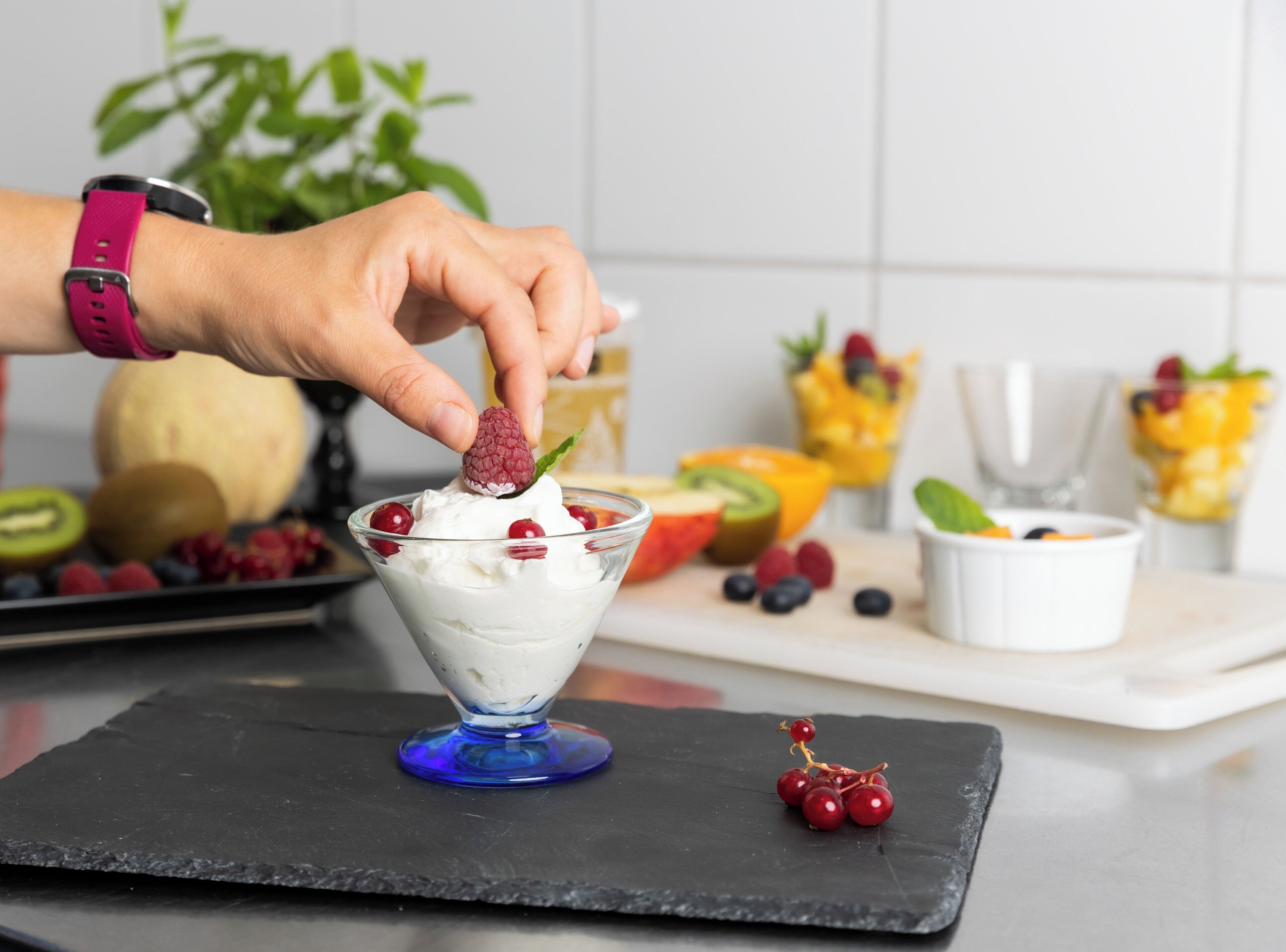A dessert in a glass bowl with whipped cream and a raspberry on a black slate.