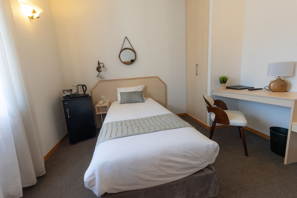 Ein Hotelzimmer mit Bett, Schreibtisch, Stuhl und einem kleinen Schrank.