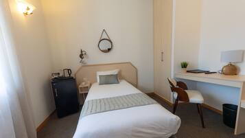 A hotel room with a bed, desk, chair, and a small cabinet.