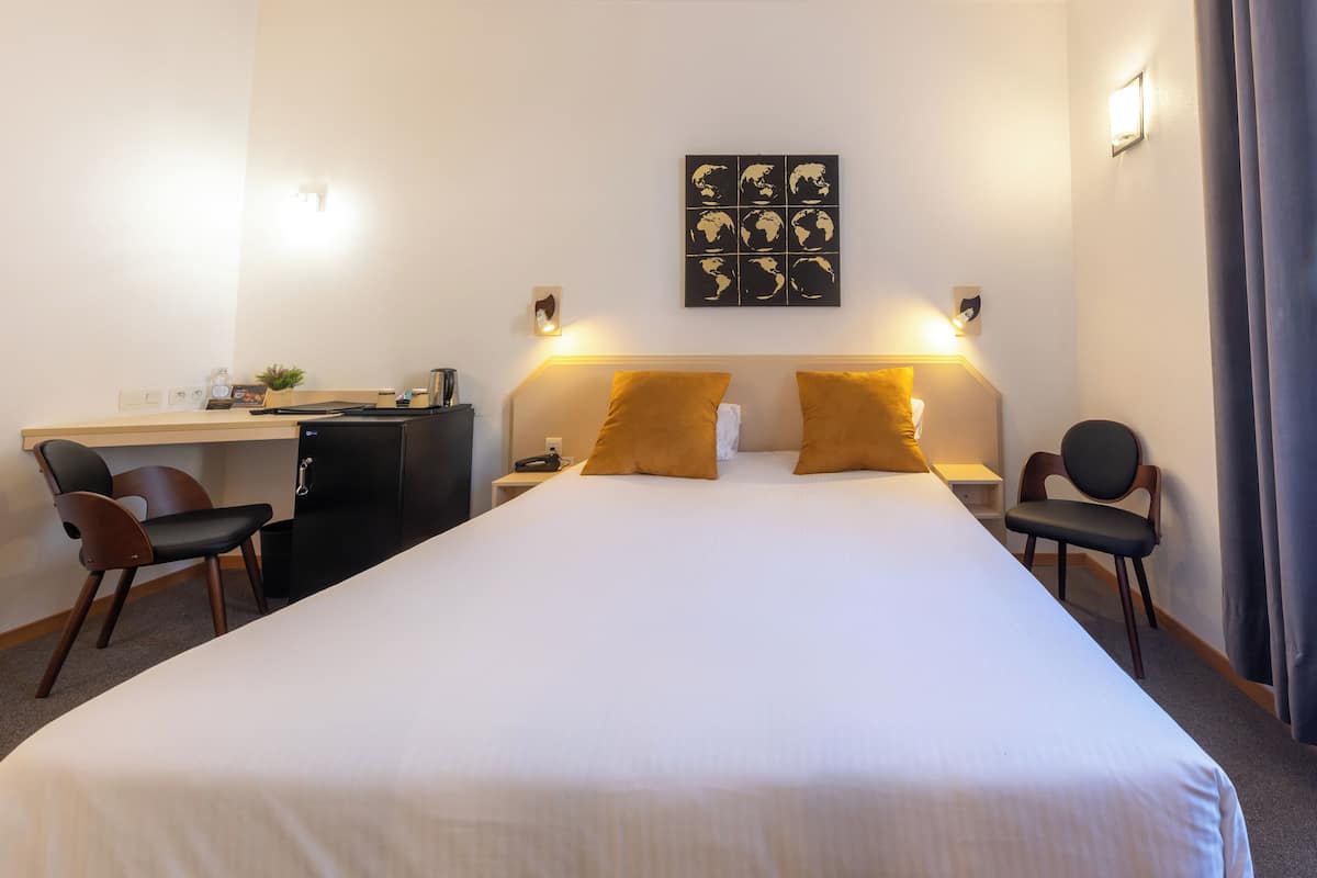 Ein Hotelzimmer mit einem großen Bett, zwei Sesseln, einem Schreibtisch und einem Wandbild einer Weltkarte.