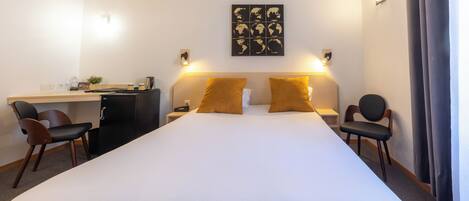 A hotel room with a large bed, two chairs, a desk, and a world map artwork on the wall.