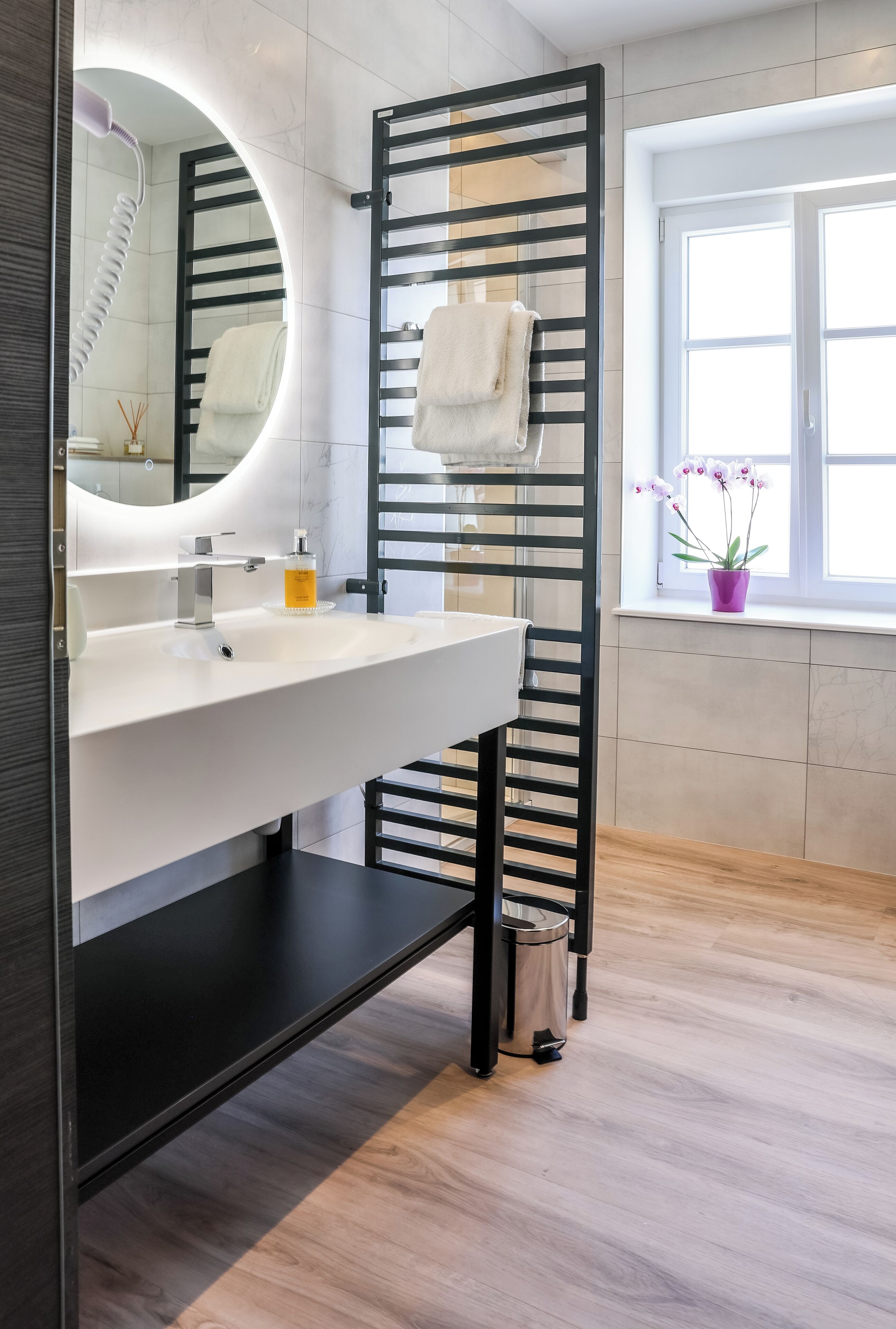 A modern bathroom with a white sink, a black towel rack, and a window with a view of the outside.