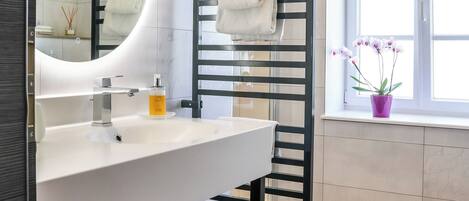 A modern bathroom with a white sink, a black towel rack, and a window with a view of the outside.
