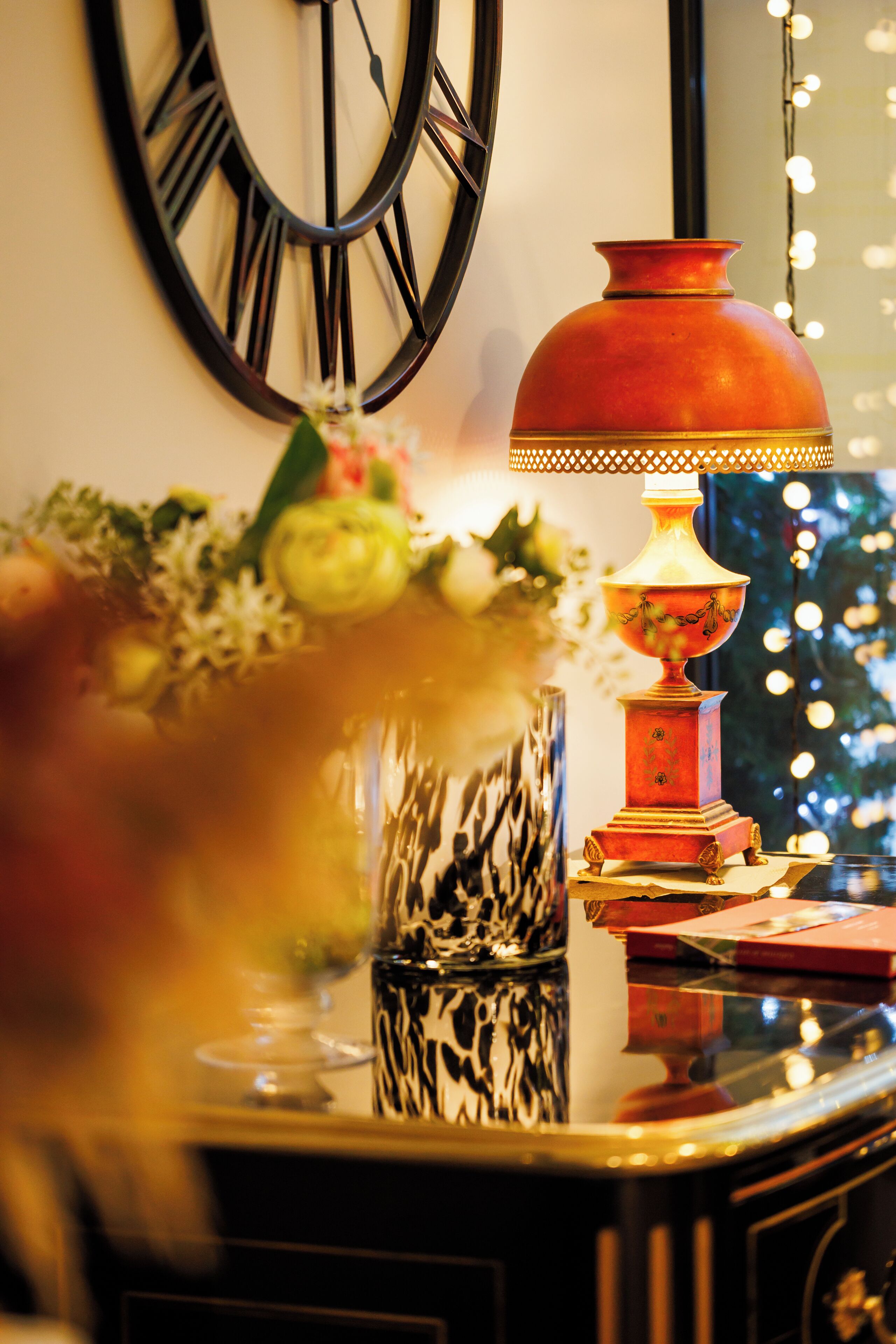 A table with a vase of flowers, a decorative lamp, and a clock on the wall.