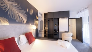 Ein modernes Hotelzimmer mit einem großen Bett, roten und weißen Kissen, einem Schrank, einer Sitzecke und einem großen Fenster.