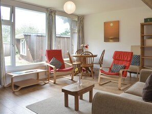 A living room with a wooden floor, a dining table with chairs, a sofa, and a bookshelf. - 2 bedroom accommodation in Mount Hawke, near Redruth (Mount Hawke, near Redruth)