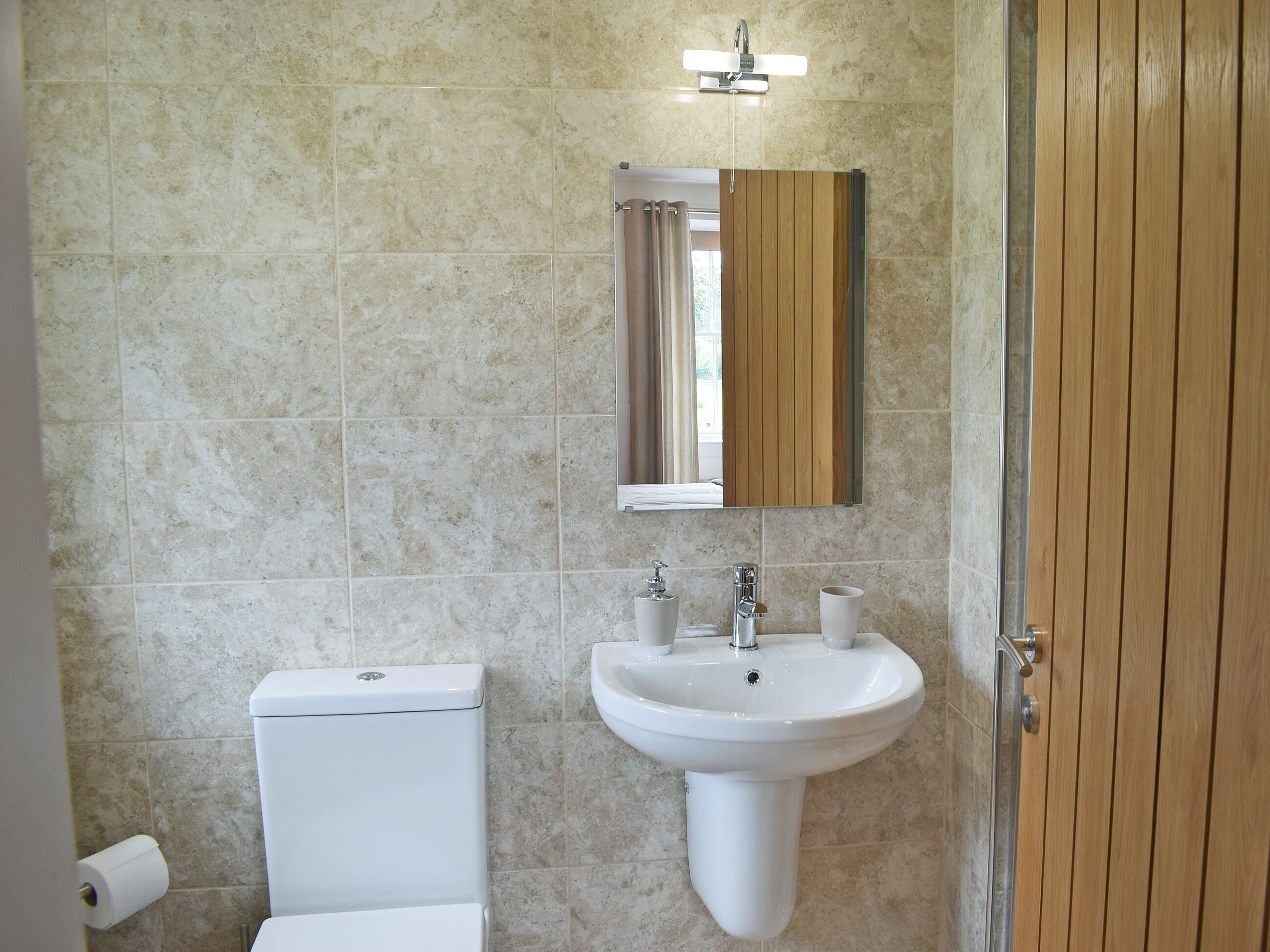 A bathroom with a toilet, sink, mirror, and wooden door.
