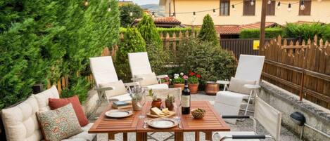A patio with a wooden table set for dining, surrounded by white chairs and a sofa.