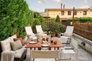 A patio with a wooden table set for dining, surrounded by white chairs and a sofa.