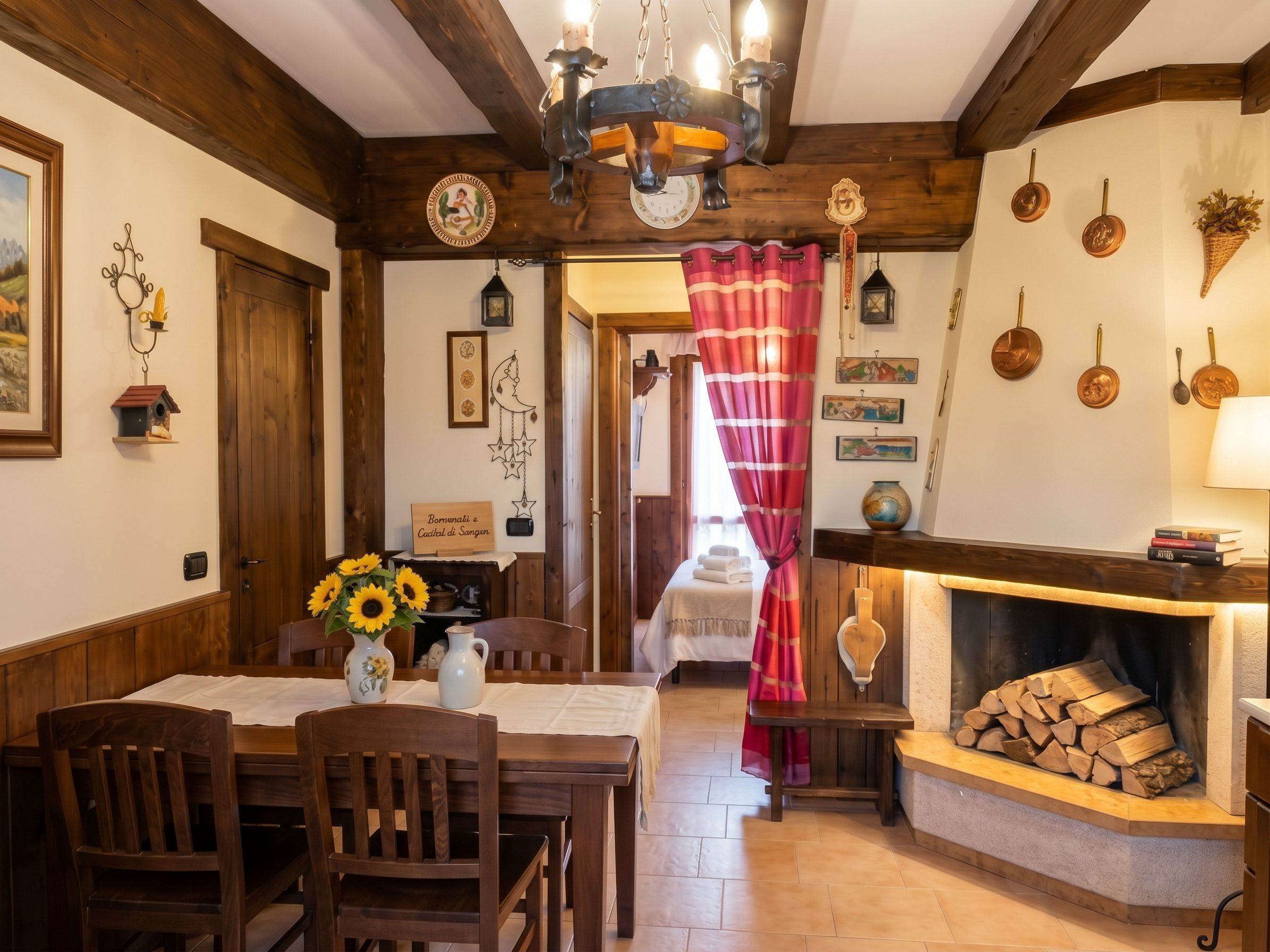 Une pièce chaleureuse avec une table à manger en bois, des chaises, une cheminée et un lit agrémenté d’un rideau rouge.