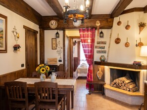 Una habitación acogedora con una mesa de comedor de madera, sillas, chimenea y una cama con cortina roja.
