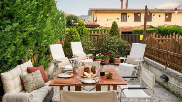 Eine Terrasse mit Holztisch, gedeckt für ein Essen, umgeben von weißen Stühlen und einer Couch.