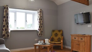 Una habitación con ventana, televisión, una silla, una mesa con tazas y una bandeja, y un armario de madera.