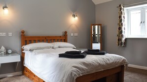 Un dormitorio con una cama de madera, dos lámparas de pared, una mesita de noche con un reloj y una ventana con cortinas.