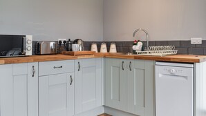 Cocina con gabinetes grises, encimera de madera, microondas, tostadora, hervidor y lavavajillas.