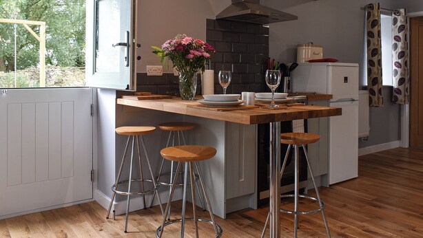 Una cocina moderna con una isla de madera, taburetes de bar, una campana extractora de acero inoxidable y vistas al exterior.