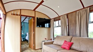 A cozy interior with a sofa, a television mounted on the wall, and a wooden door leading to another room. - Brunel Boutique Railway Carriage 5 (Dawlish Warren)