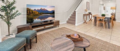 Una sala de estar moderna con un televisor de pantalla plana, una escalera, un comedor y una planta grande.