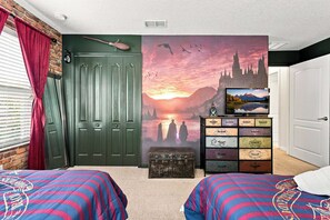A bedroom with two beds, a green door, a wall with a sunset painting, a dresser with drawers, and a window with blinds.