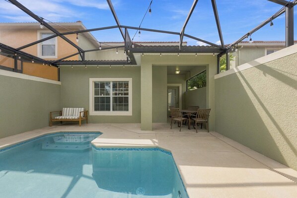 A swimming pool with a patio area, a covered seating area, and a view of a residential building.