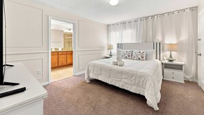 A hotel room with a bed, bedside tables, a mirror, and a view into the bathroom.