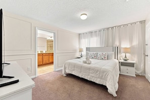 A hotel room with a bed, bedside tables, a mirror, and a view into the bathroom.