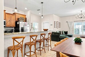 A modern kitchen with wooden cabinets, a stainless steel refrigerator, and a dining area with a wooden table and bar stools.