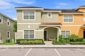 A two-story residential building with a flat roof, a front entrance with a small porch, and a parking lot in front.