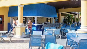 An outdoor seating area with tables and chairs, a pool, and a bar area.