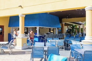 An outdoor seating area with tables and chairs, a pool, and a bar area.
