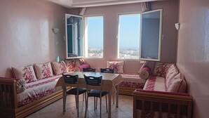 Un comedor con una mesa y sillas, un sofá con cojines estampados, y dos ventanas con cortinas.