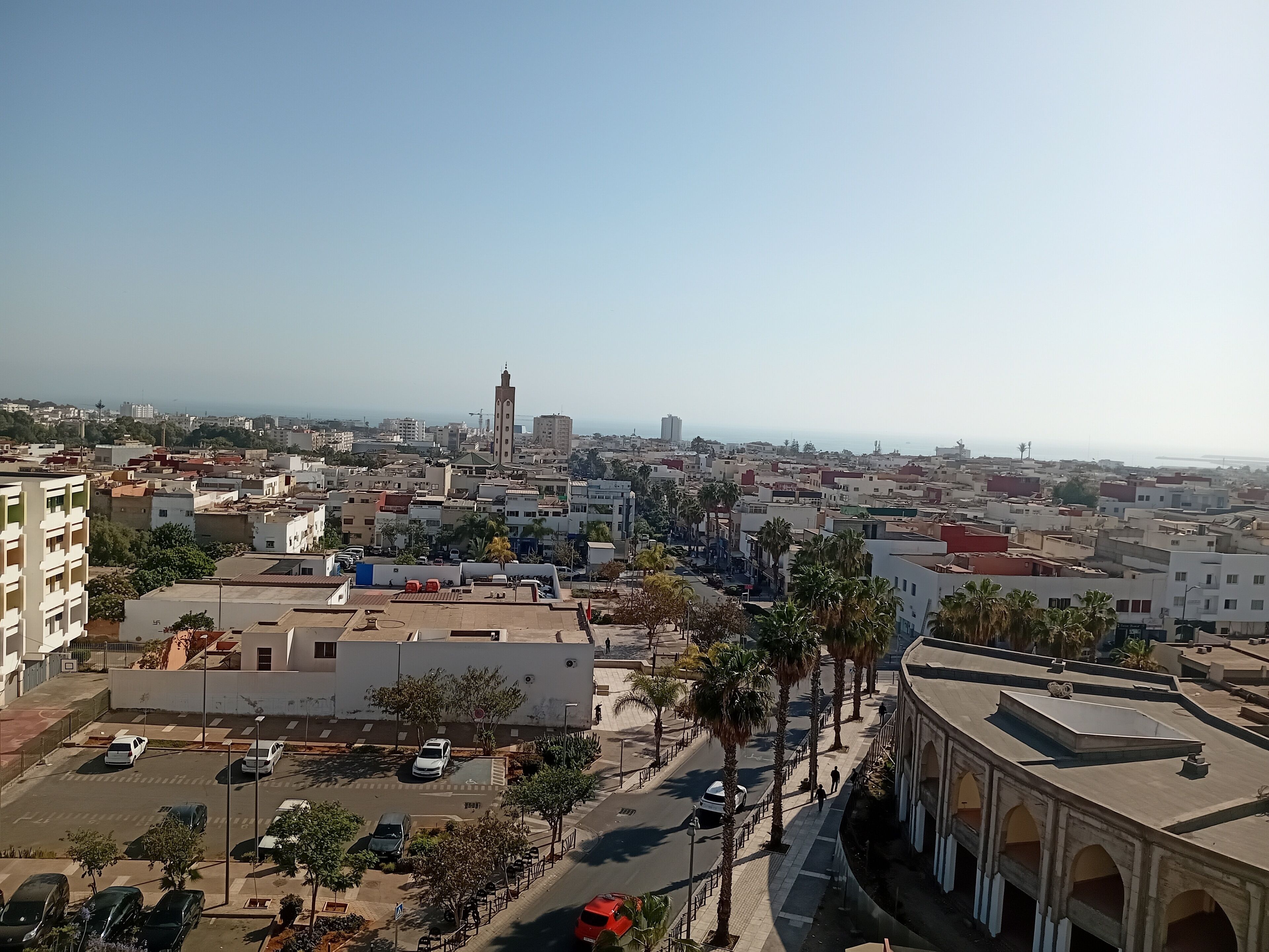 Eine Stadtansicht mit einer markanten Moschee, verschiedenen Wohngebäuden und freiem Blick auf das Meer.
