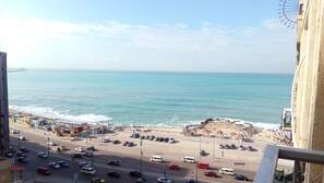 Un paysage urbain côtier avec une plage, une route où circulent des voitures et une grande roue en arrière-plan.
