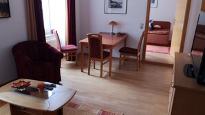 A living room with a sofa, a coffee table, a dining table with chairs, a TV, and a bed in the background. - central and beachfront apartment in Kühlungsborn East (Kühlungsborn)