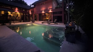 Une maison moderne dotée d’une piscine, d’un espace salon extérieur et d’une terrasse bien éclairée.