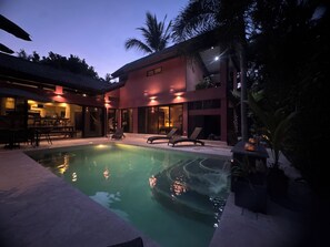Ein modernes Haus mit Swimmingpool, Sitzgelegenheiten im Freien und einer gut beleuchteten Terrasse.