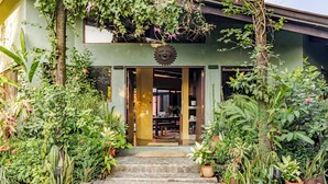 Un bâtiment écologique, orné d’une décoration en forme de soleil au-dessus de l’entrée, et entouré d’une végétation luxuriante et de plantes en pot.