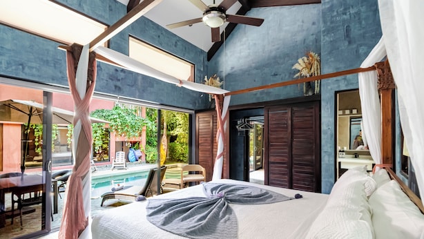 Une chambre dotée d’un grand lit, d’un ventilateur de plafond et offrant une vue sur l’espace extérieur de la piscine.