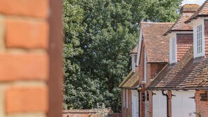 A courtyard with brick buildings, a bicycle, and potted plants. - The Coach House Stables (Hernhill)