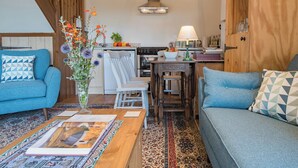 A cozy living room with a blue sofa, a wooden coffee table, and a patterned rug. - The Coach House Stables (Hernhill)