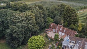 A large house with a spacious backyard, surrounded by dense trees and fields. - The Coach House Stables (Hernhill)
